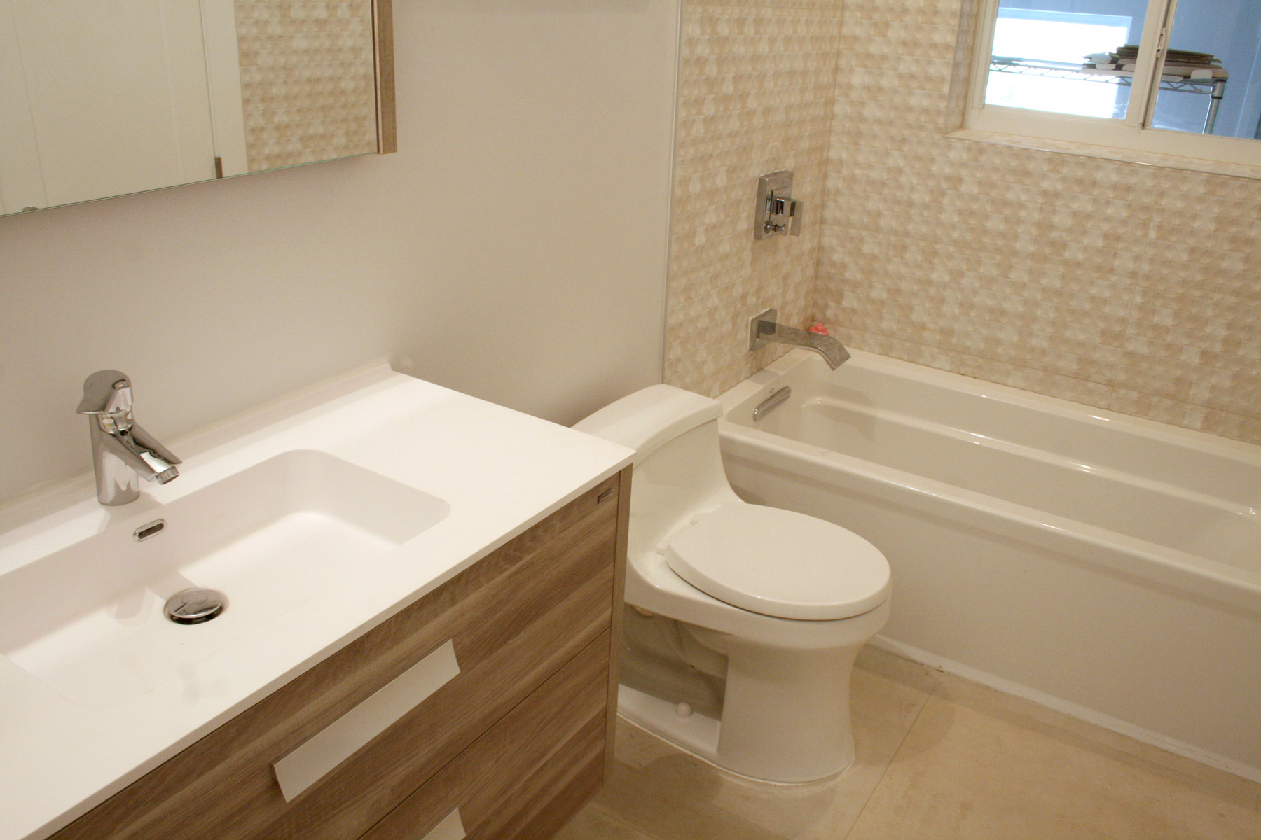 Remodeled bathroom with new wall-mounted vanity, toilet, tub and porcelain tiles