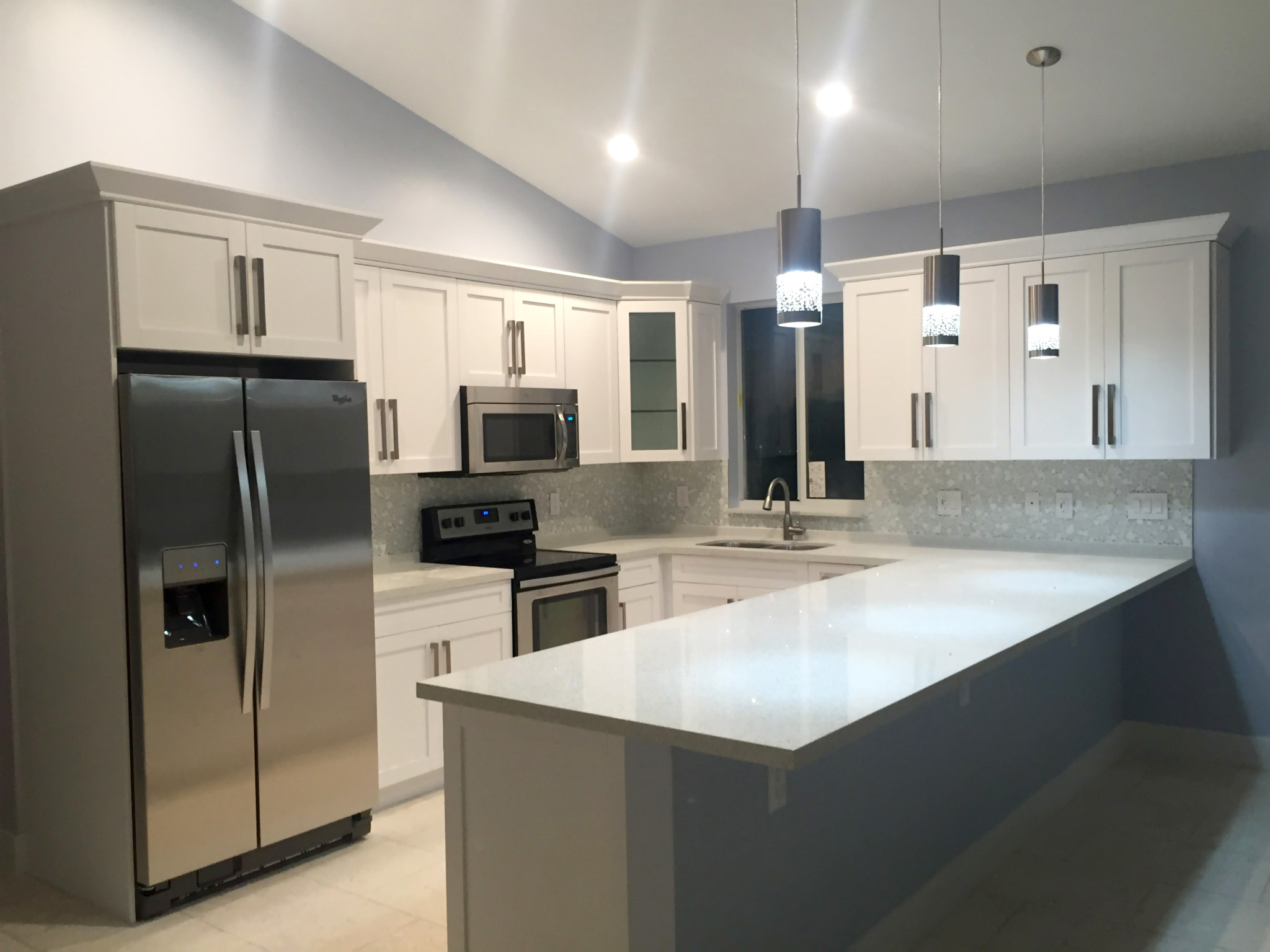 After photo of shaker style kitchen with quartz counter top, mosaic backsplash & pendant lights