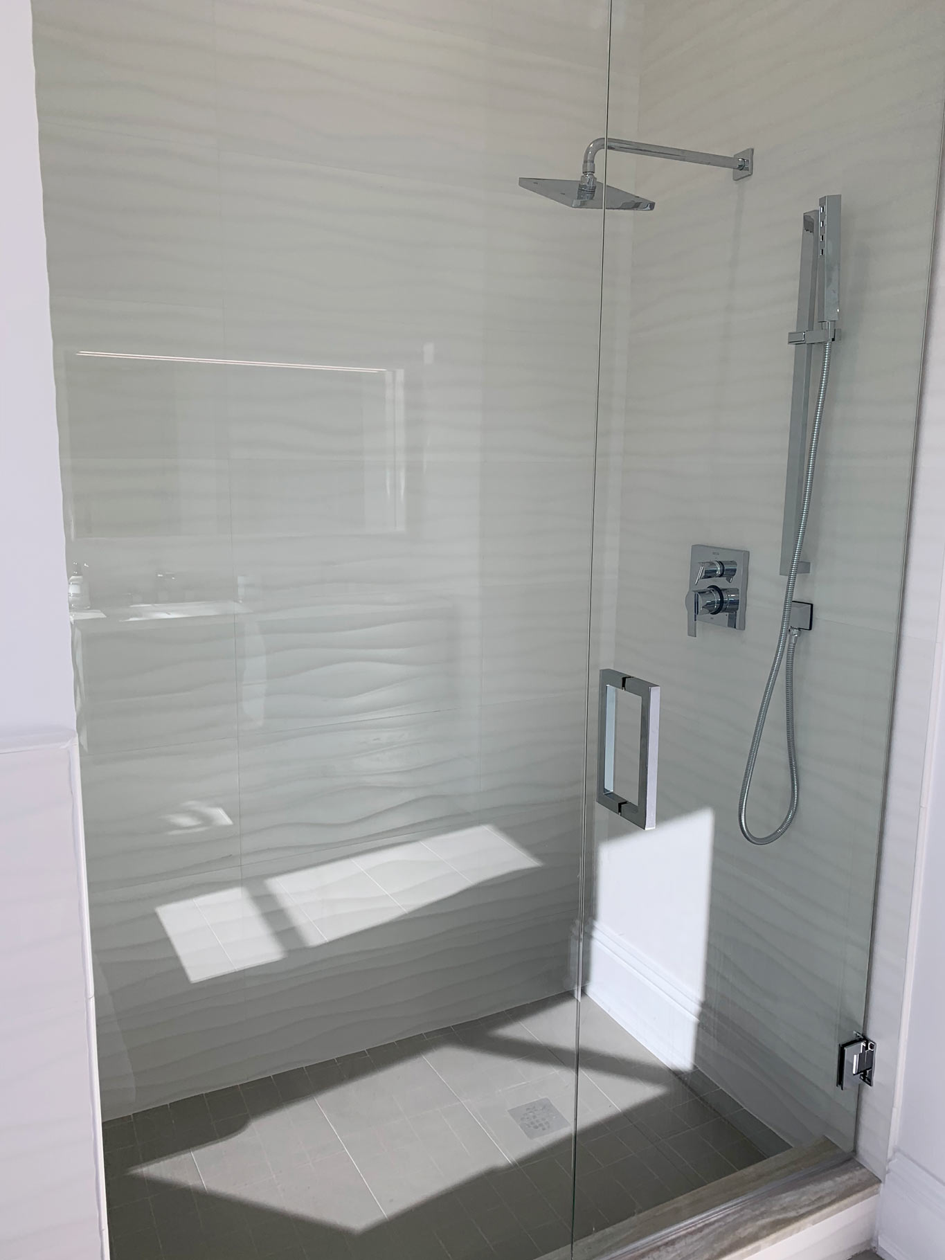 New glass shower enclosure with white stone wavy tile pattern